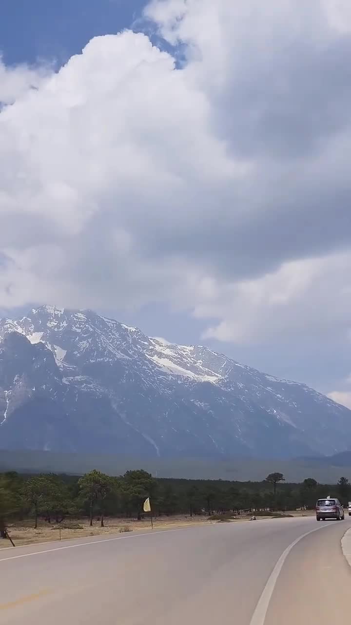 在玉龙雪山脚下，我看到了美丽的风景。周围的山的云，它是如此美丽！云层里的山白得像奶油。山下的树很壮。附近的草是黄色的，只有少数是绿色的。#玉龙雪山